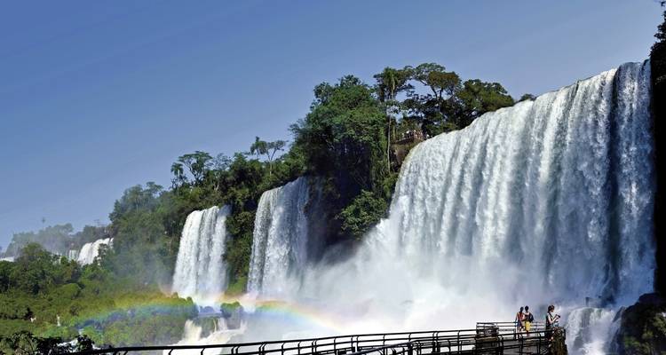 Waterfalls with rainbow and walkway with people.