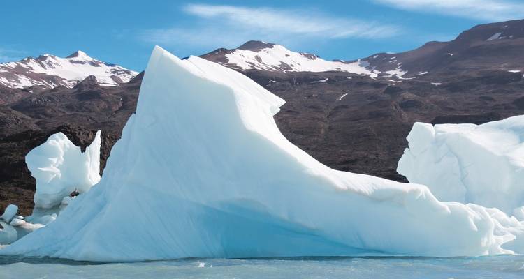 Large iceberg with snow-capped mountains in the background.