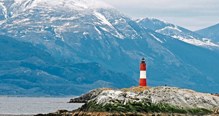 Leuchtturm auf einer felsigen Insel mit Bergen im Hintergrund.