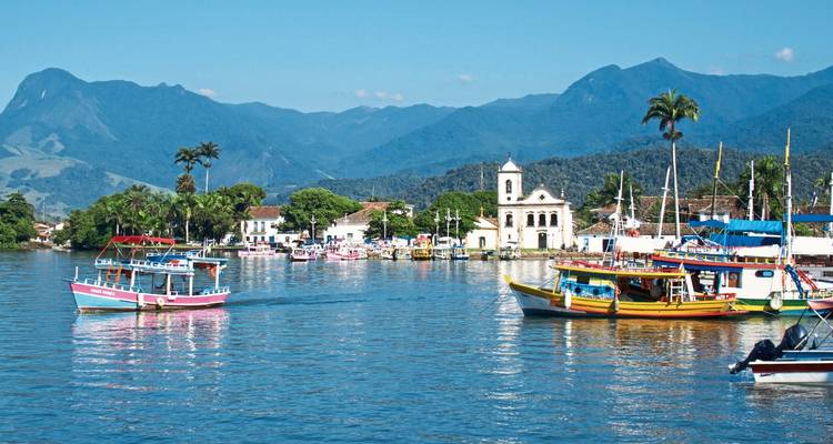 Bateaux colorés sur une voie navigable côtière sereine avec des montagnes en arrière-plan.