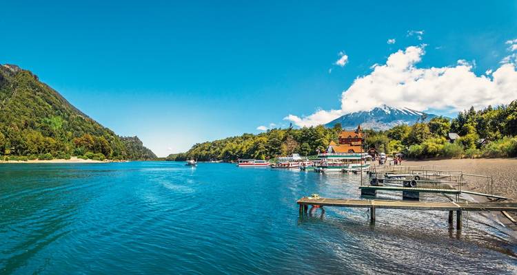Een waterkant met boten en een vulkaan op de achtergrond.