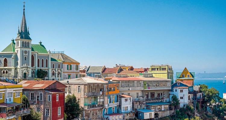 Bâtiments colorés à flanc de colline et une église surplombant l'eau.