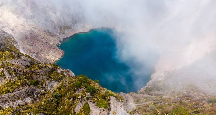 Aerial view of a volcanic crater lake partially covered by mist.