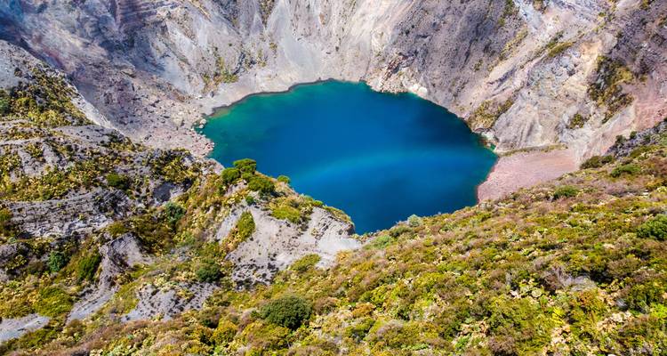 Aerial shot of a vibrant blue crater lake surrounded by steep volcanic terrain.