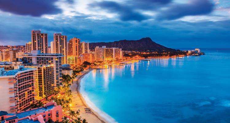 Night view of Waikiki Beach with city lights and ocean.