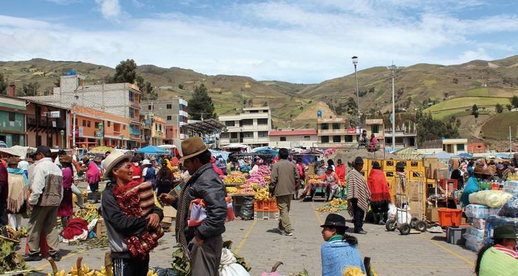 Buitenmarkt met mensen en kraampjes omringd door heuvels.