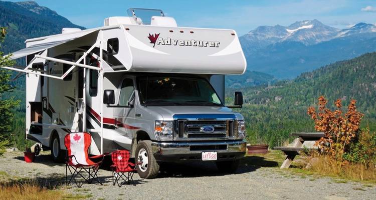 Un camping-car garé dans une région montagneuse avec des chaises installées à l'extérieur.