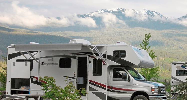 Un camping-car garé près d'une montagne pittoresque avec des arbres et des nuages.