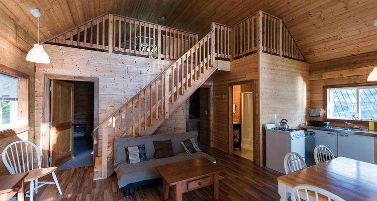 Interior of a wooden cabin with a staircase, kitchen, and dining area.