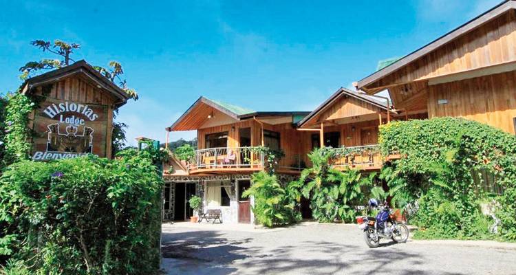 Een rustieke lodge omringd door groen, met een motorfiets geparkeerd ervoor.