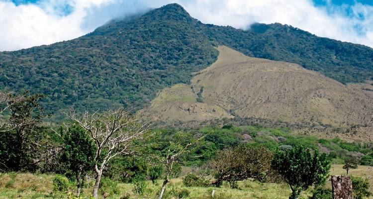 Een berglandschap met groene heuvels en bewolkte luchten.
