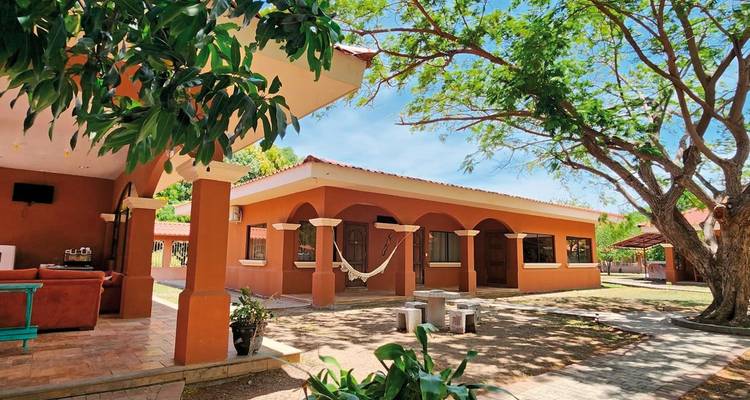 Een binnenplaats met gebouwen en een hangmat onder een boom.