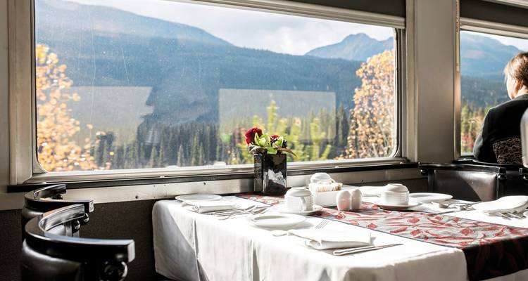 Table de salle à manger installée dans un train avec une vue panoramique sur les montagnes.