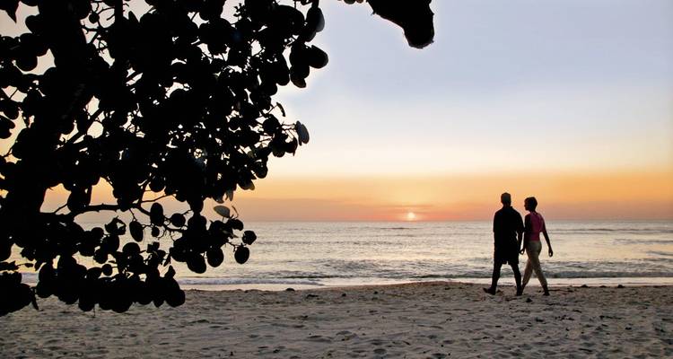 Pareja en silueta caminando por la playa de arena al atardecer colorido.