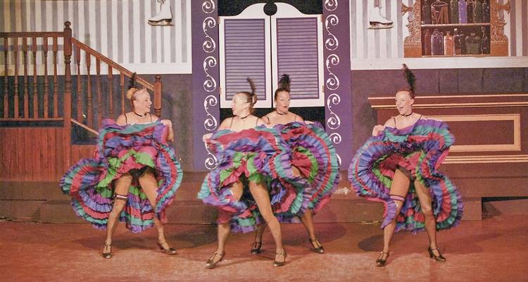Groep dansers in kleurrijke kostuums die optreden op het podium.