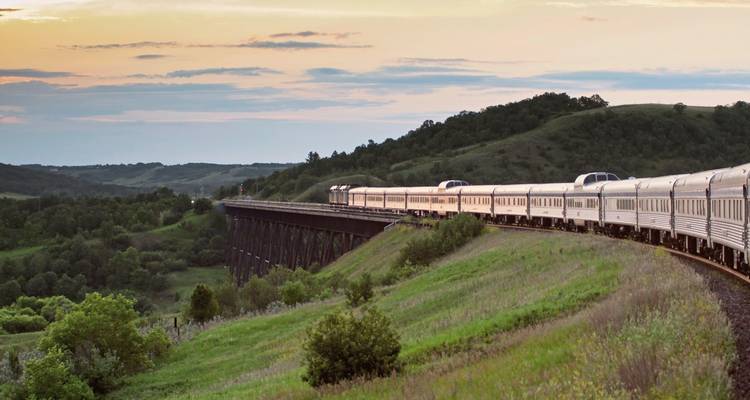 Train circulant sur des voies surélevées à travers une campagne pittoresque au coucher du soleil.