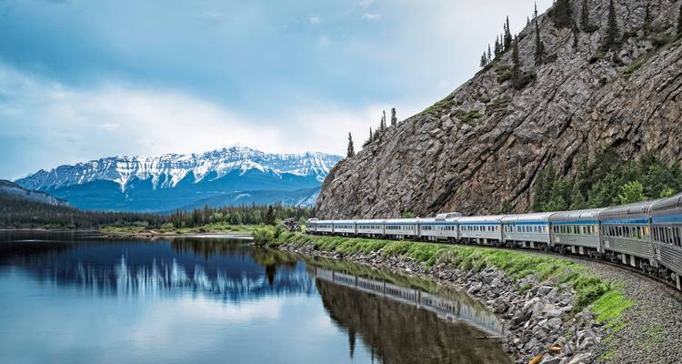 Train voyageant le long d'un lac de montagne pittoresque avec des montagnes enneigées.