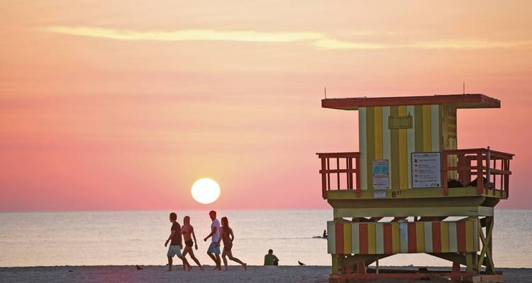 Scène de plage au coucher du soleil avec des gens et une tour de sauveteur.