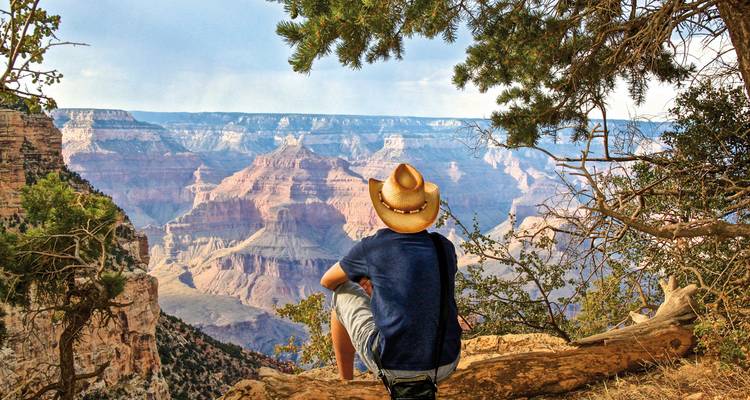 Personne assise au bord d'une falaise surplombant un vaste paysage de canyon.