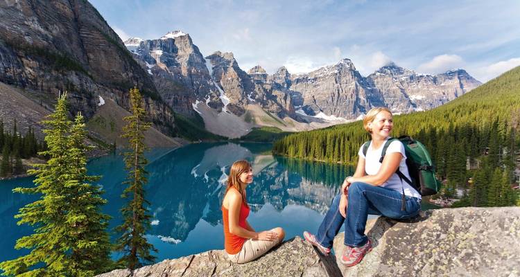 Two people sitting on rocks overlooking a vibrant blue alpine lake.