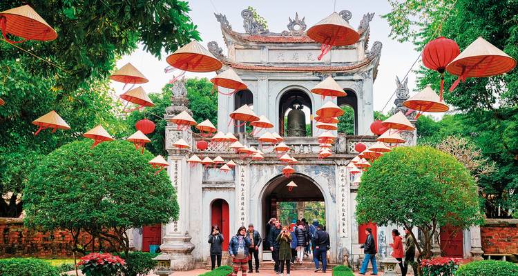 Touristes visitant le Temple de la Littérature à Hanoï avec des chapeaux traditionnels suspendus.