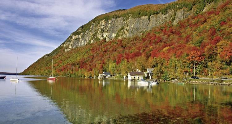 Autumnal landscape with a serene lake and colorful foliage on a rocky cliff.