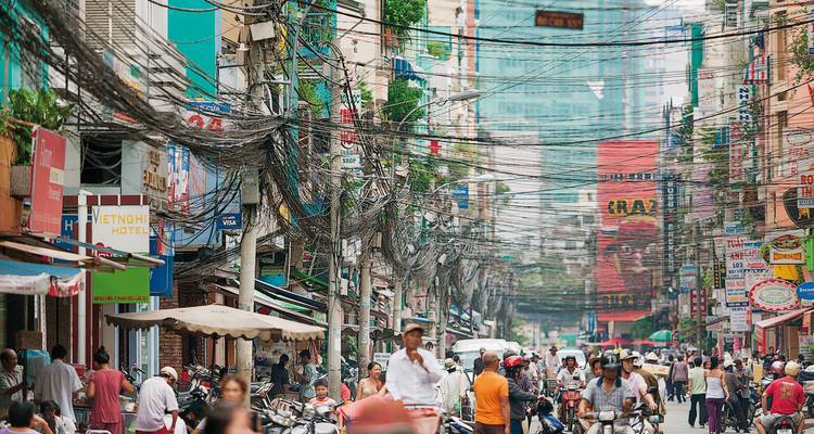 Rue urbaine animée remplie de gens, de voitures et de câbles suspendus.