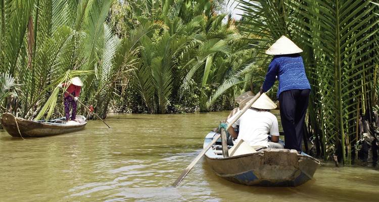 Des gens pagayant dans des embarcations à travers des voies navigables tropicales luxuriantes.