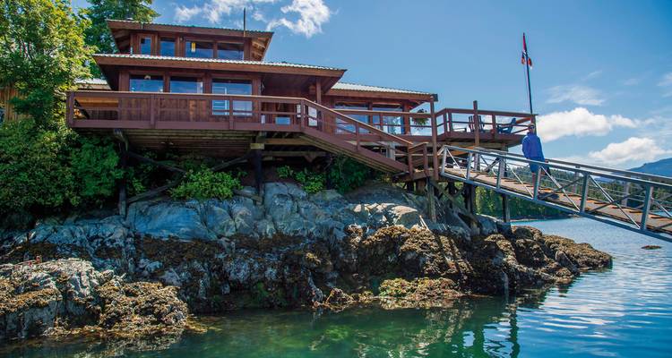 Een houten huis op een rotsachtige oever met een houten loopbrug.