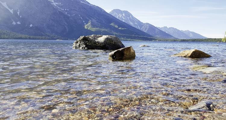 Rocks in clear lake water with mountains in the background.