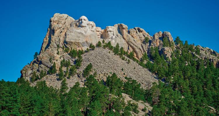 Le Mont Rushmore avec un ciel bleu dégagé et la forêt environnante.