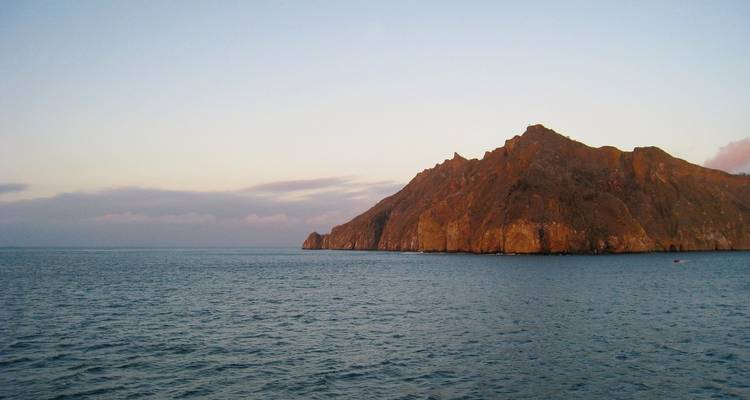 Rotsachtig eiland dat uitsteekt uit de oceaan tijdens zonsondergang.