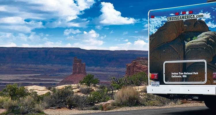 RV with a desert landscape and rock formations in the background.