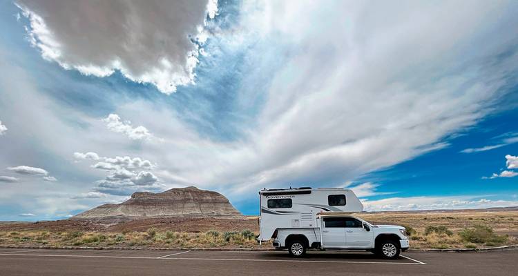 Truck camper with dramatic clouds and a blue sky in a desert setting.