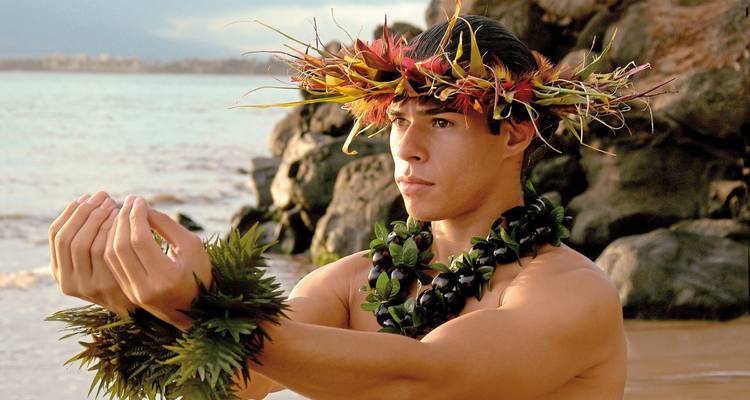 Person wearing a traditional flower crown on a beach.