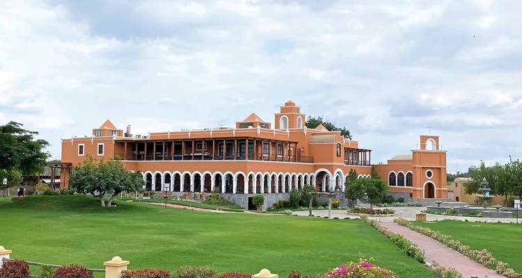 Ein großes, orangefarbenes Gebäude im Kolonialstil mit zahlreichen Bögen und einem gepflegten Rasen davor.