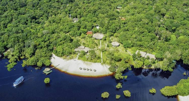 Vue aérienne d'un complexe hôtelier au bord d'une rivière entouré d'une forêt luxuriante.