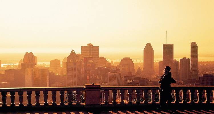 Silhouettierter Besucher genießt einen diesigen Sonnenaufgang über Montreals Skyline von einer erhöhten Terrasse.