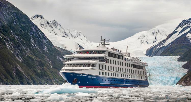 Een groot cruiseschip dat navigeert tussen ijzige wateren met besneeuwde bergen op de achtergrond.