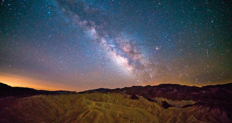 Ciel nocturne avec la Voie lactée au-dessus d'un paysage montagneux accidenté.