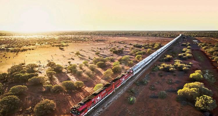 A train moving through a vast, arid landscape at sunset.