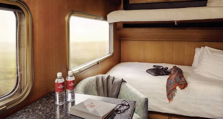 Interior of a train cabin with twin beds and a scenic view outside.