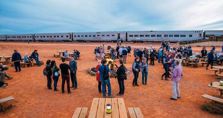 A group of people gathered near a train on a desert landscape.