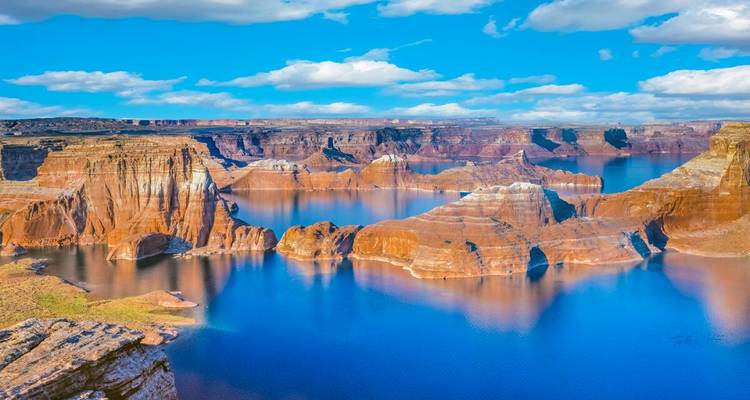 Las aguas de un azul cristalino llenan los dramáticos cañones de arenisca del lago Powell bajo nubes dispersas.