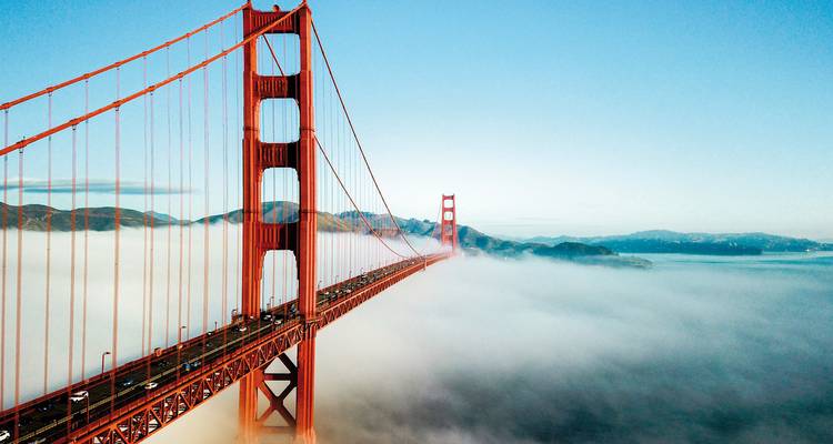 Golden Gate Bridge towering above the fog with city skyline.