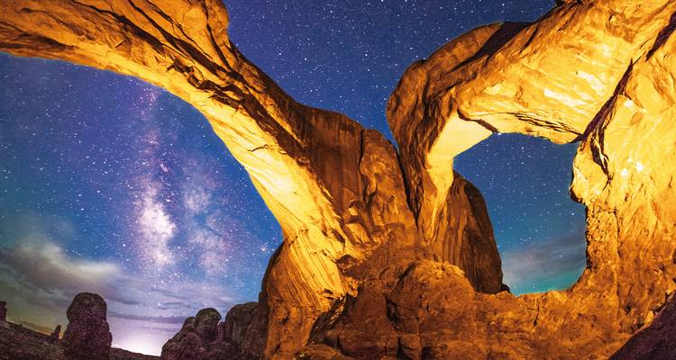 Starry night sky seen through the arch of a rock formation.