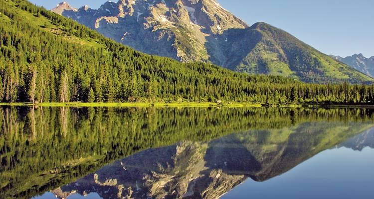 Montagnes se reflétant dans un lac calme et miroir entouré d'une forêt.
