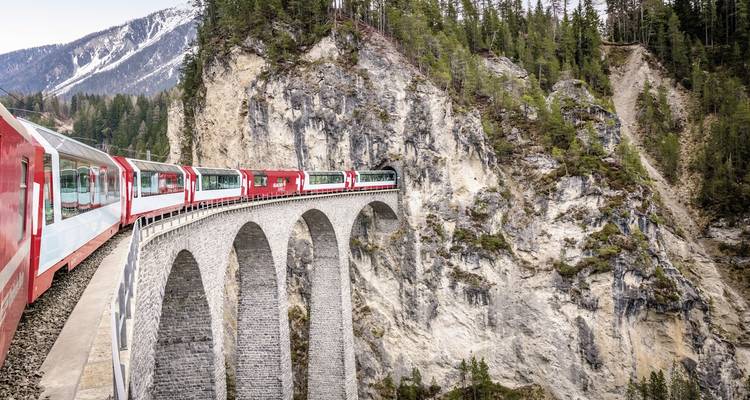Scenic train crossing a high bridge over a dramatic gorge.