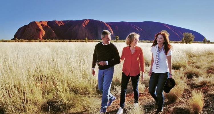 Drei Menschen gehen in einem Feld mit einer großen Felsformation im Hintergrund.