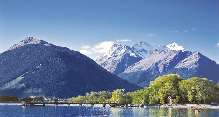 Un lac tranquille avec un quai et des montagnes enneigées au loin.
